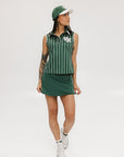 A female model wearing a sleeveless green pinstripe polo top with an applique logo on the chest and a matching green skirt, paired with a green cap.
