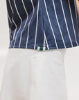 A woman wearing a sleeveless navy blue and white striped Moore Polo golf top with a cap and a white skirt.