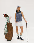 A woman wearing a sleeveless navy blue and white striped Moore Polo golf top with a cap and a white skirt.