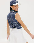 A woman wearing a sleeveless navy blue and white striped Moore Polo golf top with a cap and a white skirt.