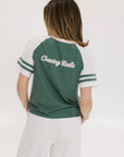 A woman wearing a green and white boxy fit t-shirt with the number 04 on the front and bold lettering on the back, along with striped sleeves.