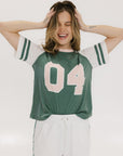 A woman wearing a green and white boxy fit t-shirt with the number 04 on the front and bold lettering on the back, along with striped sleeves.