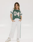 A woman wearing a green and white boxy fit t-shirt with the number 04 on the front and bold lettering on the back, along with striped sleeves.