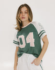 A woman wearing a green and white boxy fit t-shirt with the number 04 on the front and bold lettering on the back, along with striped sleeves.