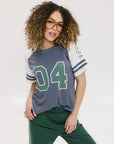 A woman wearing a blue and white striped t-shirt with the number '04' on it, paired with green pants.