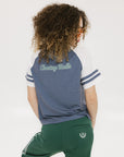 A woman wearing a blue and white striped t-shirt with the words 'chasing balls' on it, paired with green pants.