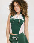 A female model wearing a sleeveless green and pink colorblocked mock neck top with mesh accents and a flat drawstring cord.