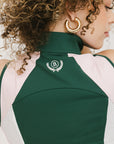 A female model wearing a sleeveless green and pink colorblocked mock neck top with mesh accents and a flat drawstring cord.