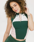 A female model wearing a sleeveless green and pink colorblocked mock neck top with mesh accents and a flat drawstring cord.