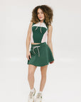 A female model wearing a sleeveless green and pink colorblocked mock neck top with mesh accents and a flat drawstring cord.