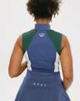 A woman wearing a sleeveless colorblocked mock neck tank top in blue and green with mesh accents and a flat drawstring cord.