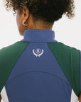 A woman wearing a sleeveless colorblocked mock neck tank top in blue and green with mesh accents and a flat drawstring cord.