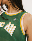 A female model wearing a green sleeveless tank top with 'Fore All' text and a logo on the chest, ribbed armholes, and a round neckline.