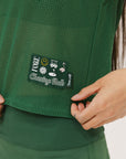 A female model wearing a green sleeveless tank top with 'Fore All' text and a logo on the chest, ribbed armholes, and a round neckline.