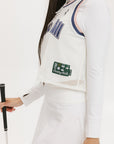 A woman wearing a white sleeveless tank top with 'Fore All' text and a flamingo logo on the chest, paired with a white skirt.