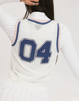 A woman wearing a white sleeveless tank top with '04' text and a flamingo logo on the chest, paired with a white skirt.
