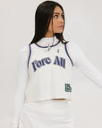 A woman wearing a white sleeveless tank top with 'Fore All' text and a flamingo logo on the chest, paired with a white skirt.