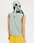 A woman wearing a green striped seersucker polo top with a collar, sleeveless with front yoke and piping accents, paired with a yellow skirt and a matching green cap.
