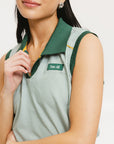 A woman wearing a green striped seersucker polo top with a collar, sleeveless with front yoke and piping accents, paired with a yellow skirt and a matching green cap.