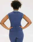 A person viewed from the back wearing a sleeveless polo shirt in blue with white collar and green trim, paired with matching pants.