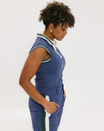 A woman wearing a sleeveless indigo blue polo with a striped collar and v-neck.