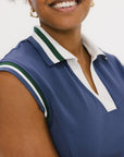 A woman wearing a sleeveless indigo blue polo with a striped collar and v-neck.