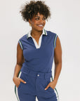 A woman wearing a sleeveless indigo blue polo with a striped collar and v-neck.