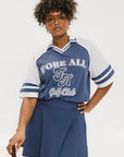 A person wearing a blue and white rugby-inspired polo shirt with Mesh body appliqué logos, a ribbed collar and placket, and elastic toggles at the side seam hem. The shirt has 'FORE ALL' text and a golf club logo on the front.