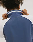 A person wearing a blue and white rugby-inspired polo shirt with Mesh body appliqué logos, a ribbed collar and placket, and elastic toggles at the side seam hem. The shirt has 'FORE ALL' text and a golf club logo on the front.