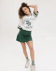 A woman wearing a white rugby-inspired polo shirt with green details and text that reads 'FORE Golf Club'.