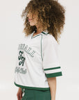 A woman wearing a white rugby-inspired polo shirt with green details and text that reads 'FORE Golf Club'.