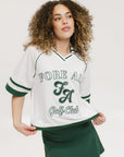 A woman wearing a white rugby-inspired polo shirt with green details and text that reads 'FORE ALL Golf Club'.