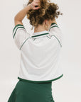 A woman wearing a white rugby-inspired polo shirt with green details and text that reads 'FORE Golf Club'.