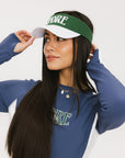 A female model wearing a long sleeve activewear top in blue and white with the text 'FORE' on the front, paired with a matching skirt and a visor with the text 'FORE'.