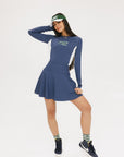 A female model wearing a long sleeve activewear top in blue and white with the text 'FORE' on the front, paired with a matching skirt and a visor with the text 'FORE'.