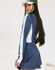 A female model wearing a long sleeve activewear top in blue and white with the text 'FORE' on the front, paired with a matching skirt and a visor with the text 'FORE'.