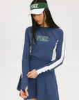 A female model wearing a long sleeve activewear top in blue and white with the text 'FORE' on the front, paired with a matching skirt and a visor with the text 'FORE'.