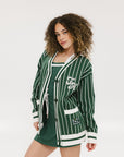 A woman modeling a pinstripe green and white cardigan with intarsia knit details, applique logos, and a button-up closure.