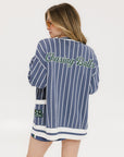 A woman wearing an oversized blue and white pinstripe cardigan with intarsia knit details and applique logos, paired with an indigo dress.