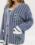 A woman wearing an oversized blue and white pinstripe cardigan with intarsia knit details and applique logos, paired with an indigo dress.