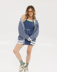 A woman wearing an oversized blue and white pinstripe cardigan with intarsia knit details and applique logos, paired with an indigo dress.