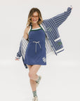 A woman wearing an oversized blue and white pinstripe cardigan with intarsia knit details and applique logos, paired with an indigo dress.
