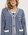 A woman wearing an oversized blue and white pinstripe cardigan with intarsia knit details and applique logos, paired with an indigo dress.