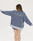 A woman wearing an oversized blue and white pinstripe cardigan with intarsia knit details and applique logos, paired with an indigo dress.