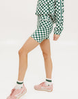 A person wearing a green and white checkered shorts and pink/green striped socks, standing against a white background.