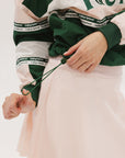 A woman wearing a green and pink racing shirt with colorblocking and text embroidery on it.