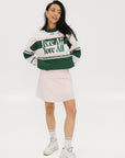 A woman wearing a green and pink racing shirt with colorblocking and text embroidery on it.