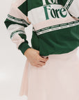 A woman wearing a green and pink racing shirt with colorblocking and text embroidery on it.