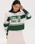 A woman wearing a green and pink racing shirt with colorblocking and text embroidery on it.