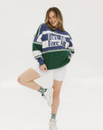 A woman wearing an indigo and green long-sleeved racing shirt with colorblocking and text embroidery.